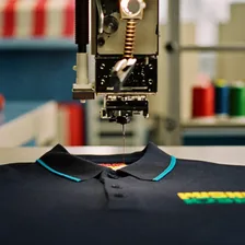 Stickmaschine stickt farbiges Garn auf ein dunkles Poloshirt